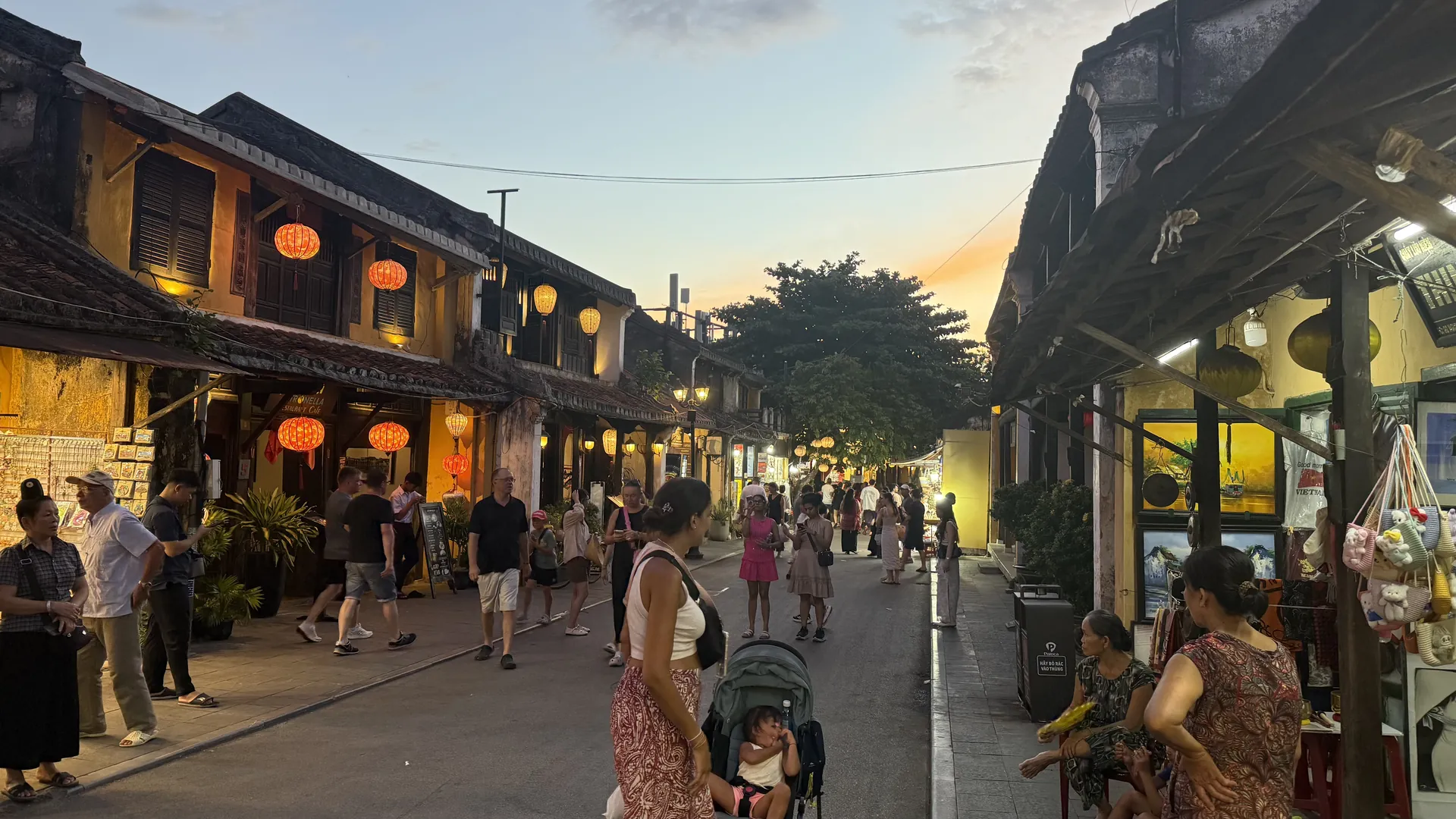 The old town of Hoi An at dusk, silk lanterns lit along the wooden shopfronts and people walking down the pedestrian street