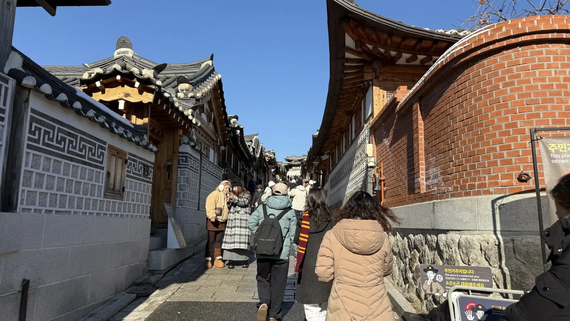 Tourists using their phones while exploring the historic Bukchon Hanok Village in Seoul, South Korea.