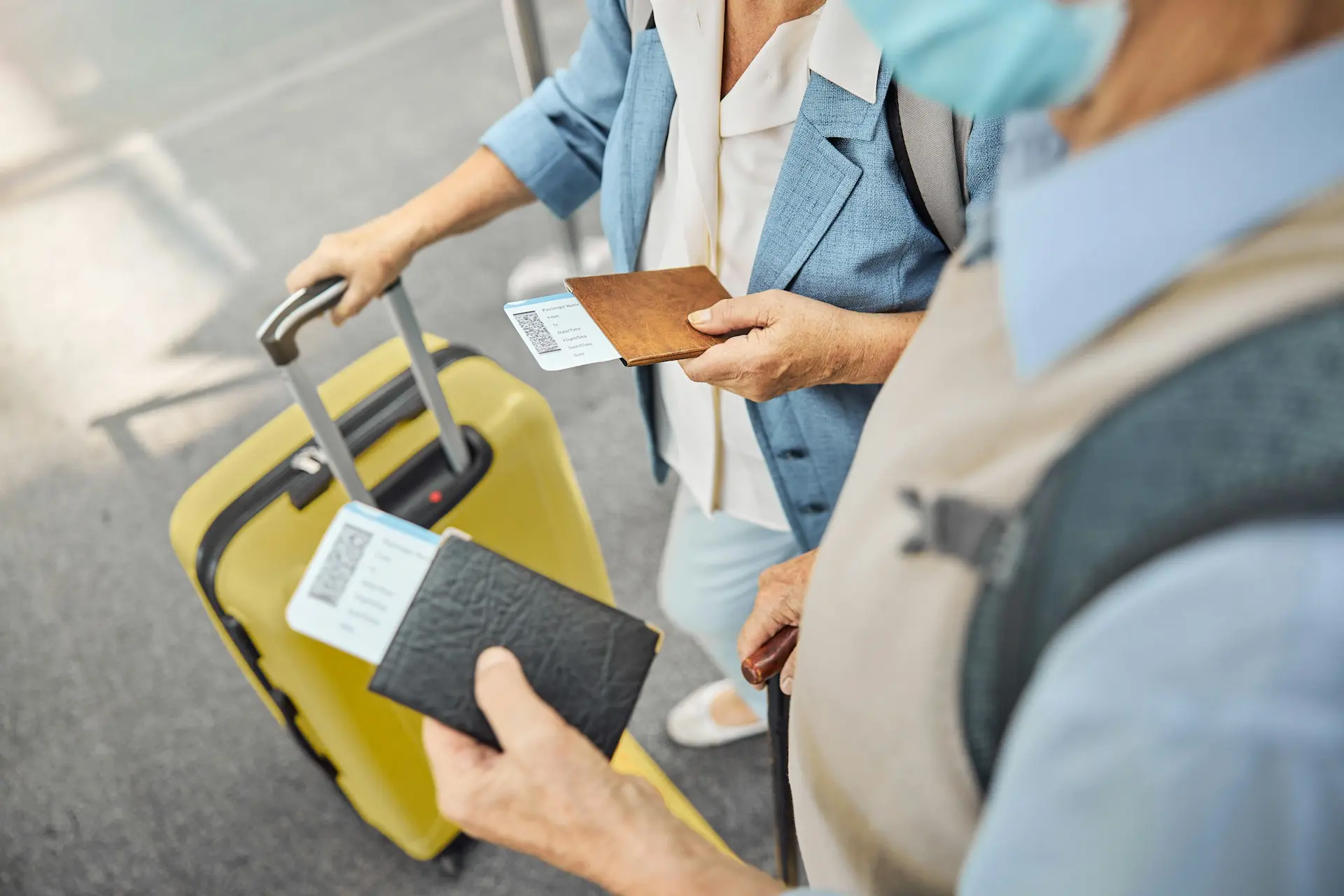 Illustration of two travellers holding their passports and flight tickets, standing near a yellow suitcase at the airport.